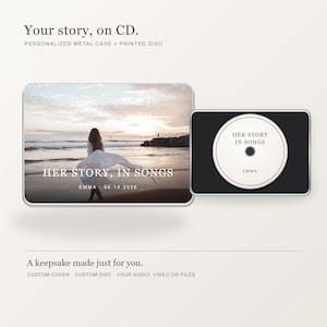 May include: A rectangular metal CD case featuring a beach sunset photograph with the text "HER STORY, IN SONGS" and "EMMA 06.14.2026". Beside it, a black case holds a white circular disc printed with "HER STORY IN SONGS" and "EMMA".