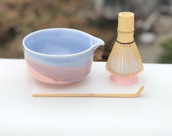 Könnte beinhalten: Ein Matcha-Teeset mit einer pastellfarbenen Schale, einem Bambusbesen und einem Bambuslöffel. Die Schale ist hellblau, rosa und lila. Der Schneebesen ist beige mit rosa Basis. Der Löffel ist hellbraun.