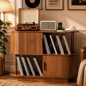 May include: A mid-century modern wooden record player console with tambour sliding doors, featuring a brown suitcase-style turntable, a cream-colored speaker, a wireless charging pad, and multiple vinyl records stored in vertical slots.