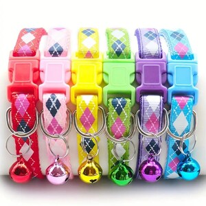 May include: Six brightly coloured pet collars, each featuring an argyle pattern on the strap and a matching plastic buckle. Each collar has a silver ring with a small, shiny bell. Colours include red, pink, yellow, green, purple, and blue.