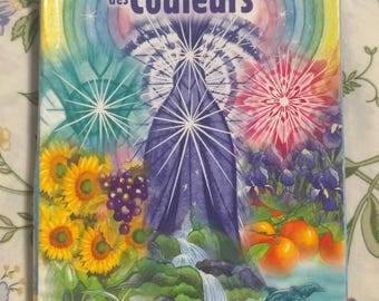 Op de afbeelding: Een kaartspel met 39 orakelkaarten getiteld L'Oracle des Couleurs. De doos toont een centrale paarse figuur, een regenboog, zonnebloemen, druiven, sinaasappels, lelies en twee dolfijnen. De tekst luidt L'Oracle des Couleurs en Vos Couleurs vous parlent de votre vie.