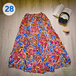 Könnte beinhalten: Langer, fließender Rock mit einem lebendigen Blumenmuster in Blau-, Rosa-, Gelb- und Orangetönen. Der Rock hat einen Kordelzug in der Taille und ein mehrschichtiges Design. Die Zahl "28" befindet sich in einem weißen Kreis oben links.
