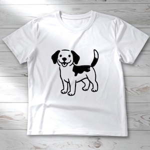 Op de afbeelding: Wit T-shirt met een zwart-witte cartoonhondenillustratie. De hond heeft zwarte oren, een zwarte vlek op zijn rug en een lachende uitdrukking. Het T-shirt is gemaakt van een zacht materiaal en heeft korte mouwen.
