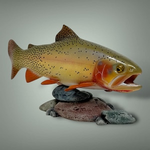 Peut inclure: Une truite en bois sculptée avec des marques orange et jaunes, perchée sur une base de roche. La truite a une apparence réaliste avec des écailles détaillées et une bouche légèrement ouverte.