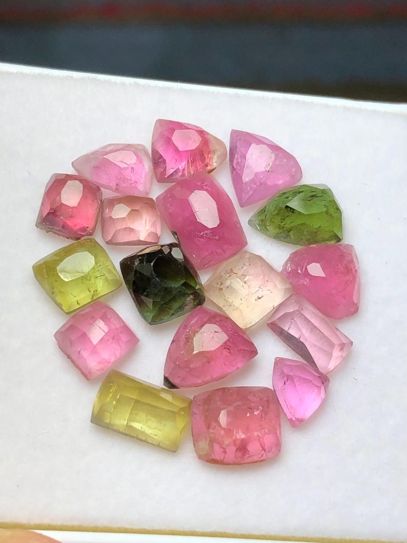 May include: A collection of faceted gemstones in various colors, including pink, green, yellow, and clear. The gemstones are arranged closely together, showcasing their different shapes and internal structures. The gems are likely tourmaline.