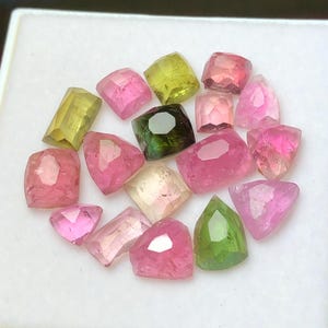May include: A collection of faceted gemstones in various shapes and colors, including pink, green, and yellow. The gems are displayed on a white surface, showcasing their clarity and brilliance. These gemstones are ideal for jewelry making.