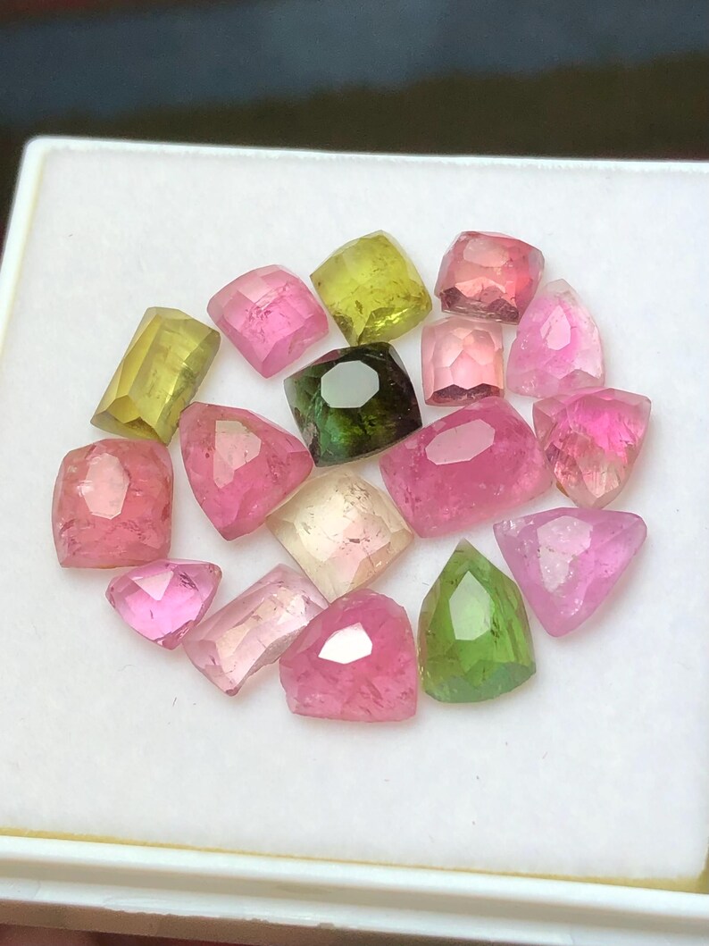May include: A collection of faceted gemstones in various shapes and colors, including pink, green, and yellow. The gems are displayed on a white surface, showcasing their clarity and brilliance. These gemstones are ideal for jewelry making.
