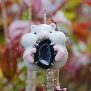 Peut inclure: Une figurine de hamster en céramique blanche fantaisiste tenant une géode noire et blanche. Le hamster a des accents roses sur les oreilles et les pattes. La géode est ovale et sertie de griffes en métal argenté.