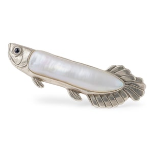 May include: A silver-toned fish-shaped brooch with a pearlescent white body. The fish has a small, dark blue eye and detailed fins. The brooch is likely made of metal and features a detailed design.