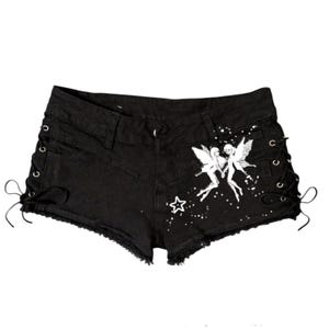 May include: Black denim shorts with frayed edges and lace-up sides. The shorts feature a white graphic of two fairies and a star. A stylish and unique addition to any wardrobe.