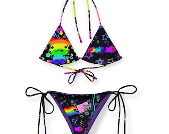 Puede incluir: Bikini de dos piezas con fondo negro y gráficos pixelados coloridos. La parte superior presenta un diseño de arcoíris y el texto "POW XD". La parte inferior tiene un gráfico de Nyan Cat y una bandera arcoíris.