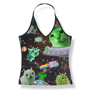 Op de afbeelding: Een zwarte haltertop met een ruimte-thema print met groene alien-katten, een vliegende schotel, een gepixelde regenboogkat en diverse sterren tegen een donkere kosmische achtergrond. Het kledingstuk heeft dunne zwarte bandjes en een V-hals.