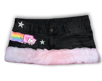 May include: Black denim mini skirt with a pink faux fur trim. The skirt features a pixelated Nyan Cat patch with a rainbow trail and two star-shaped embellishments. A button and pockets are visible.