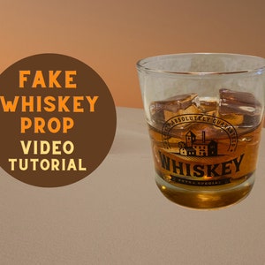 Könnte beinhalten: Ein klares Glas gefüllt mit bernsteinfarbener Flüssigkeit und Eiswürfeln, beschriftet mit "Whiskey Extra Special". Das Glas hat ein Etikett im Vintage-Stil mit einer Brennereidarstellung. Der Text "Fake Whiskey Prop Video Tutorial" ist ebenfalls zu sehen.