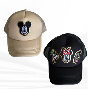May include: Two baseball caps. One is tan with a Mickey Mouse patch. The other is black with patches of Minnie Mouse, Donald Duck, and Goofy. Both caps have mesh backs and curved visors.