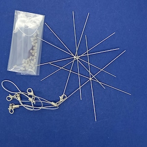 May include: Jewellery-making supplies on a blue backdrop. The image shows silver-coloured metal wires, small rectangular beads in a clear plastic bag, and several silver-coloured chain necklaces with clasps.
