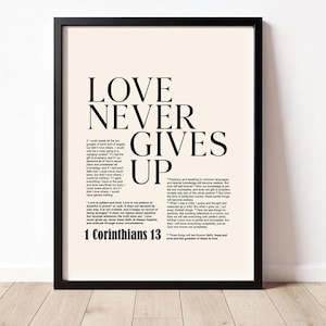 Peut inclure: Impression d'art encadrée avec les mots "LOVE NEVER GIVES UP" en gros caractères noirs. L'impression comprend le texte de 1 Corinthiens 13 en plus petit. Le fond est beige clair.