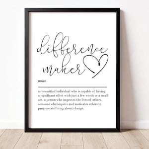 May include: Black framed print with the words "difference maker" in a cursive font, with a heart symbol. Below, the definition of "difference maker" is printed in a simple, easy-to-read font. The print is displayed on a white wall.