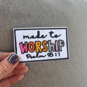 May include: A white rectangular patch with the words "made to WORSHIP" in colorful, playful lettering. Below, the text "Psalm 95:1" is written in a smaller, black font. The patch has a black border.