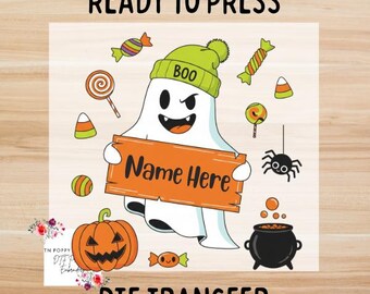 May include: A Halloween-themed DTF transfer design featuring a cartoon ghost wearing a green beanie with "BOO" on it, holding an orange sign that says "Name Here". The design includes a jack-o'-lantern, candy, and a spider.