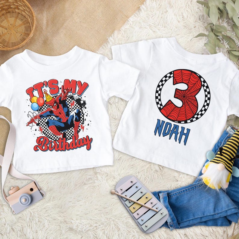 Puede incluir: Dos camisetas blancas con dise&ntilde;os de Spider-Man. Una dice "IT'S MY Birthday" con una ilustraci&oacute;n de Spider-Man. La otra tiene el n&uacute;mero 3 con un dise&ntilde;o de telara&ntilde;a y el nombre "NOAH" en azul.