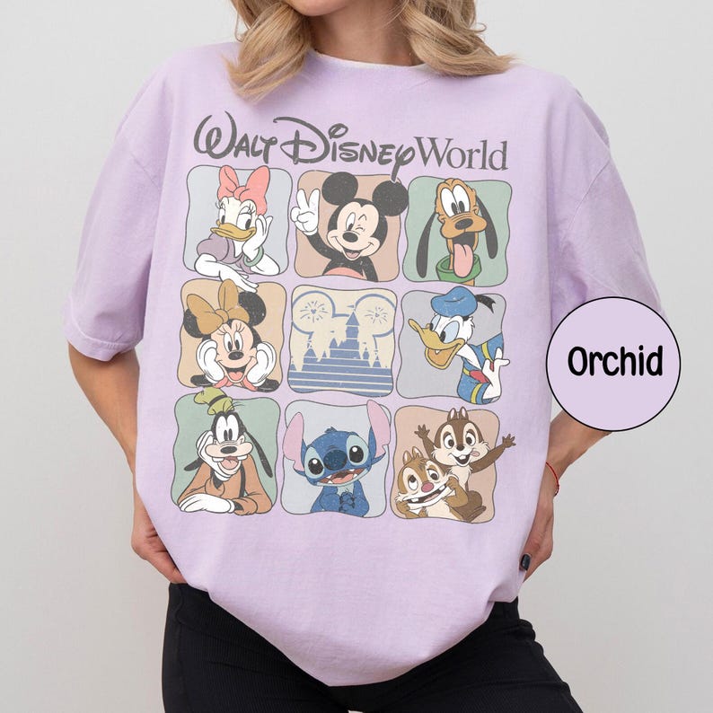 Pu&ograve; includere: Una maglietta lilla con una griglia di personaggi Disney, tra cui Topolino, Minnie, Paperino e Pippo. Le parole "Walt Disney World" sono arcuate nella parte superiore. Un adesivo rotondo con la parola "Orchid" &egrave; a destra.
