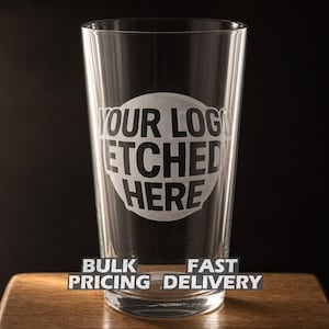 May include: A clear pint glass with the text "YOUR LOGO ETCHED HERE" in a white circle. The glass is on a wooden surface against a black background. The words "BULK PRICING FAST DELIVERY" are below the glass.