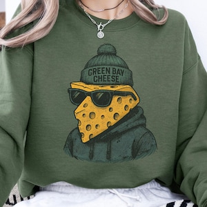 May include: Green sweatshirt featuring a graphic of a cheese wedge wearing sunglasses and a green beanie with the text "GREEN BAY CHEESE". The cheese character is wearing a green hoodie.