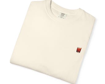 Könnte beinhalten: Gefaltetes cremefarbenes T-Shirt mit einem kleinen, gestickten Cocktailglas. Das Glas, gefüllt mit roter Flüssigkeit und Eis, befindet sich auf der Vorderseite. Das T-Shirt hat einen Rundhalsausschnitt und ein Comfort Colors-Markenschild.