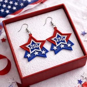 May include: A pair of star-shaped earrings in a red, white, and blue color scheme, with the number "250" in the center. The earrings are displayed in a red box with a white interior. The earrings have silver hooks.