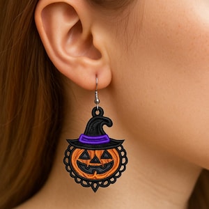 Puede incluir: Un par de pendientes con temática de Halloween. Cada pendiente presenta una calabaza sonriente con un sombrero de bruja negro y una banda morada. La calabaza naranja tiene un borde de encaje negro y está suspendida de un gancho plateado.