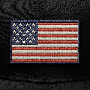 May include: Embroidered patch featuring the American flag. The patch has a blue rectangle with white stars in the upper left corner and red and white stripes. The patch is rectangular and has a dark blue border.