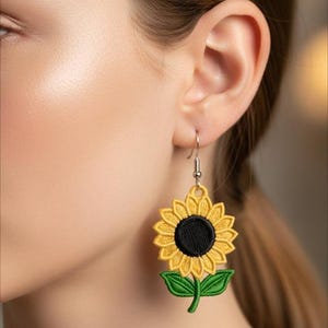 Peut inclure: Boucles d'oreilles brodées en forme de tournesol, avec des pétales jaunes, un centre noir et des feuilles vertes. Les boucles d'oreilles sont suspendues à des crochets argentés. Accessoire floral détaillé.