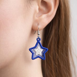 May include: A single star-shaped earring with a blue outline and a white, textured interior. The earring is suspended from a silver-colored hook. The star design is a patriotic theme, suitable for holidays or everyday wear.