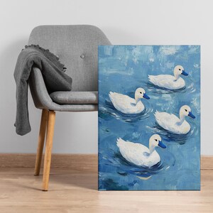 May include: An oil painting on canvas depicting four white ducks with blue beaks on a blue water background. The artwork is propped up next to a grey chair with a grey blanket draped over it.