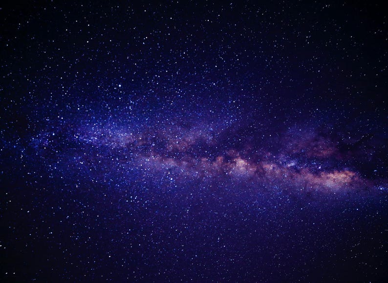 May include: A vibrant image of the night sky, showcasing a deep blue expanse dotted with countless stars. The Milky Way galaxy stretches across the frame, with hues of purple and pink, creating a stunning celestial display.