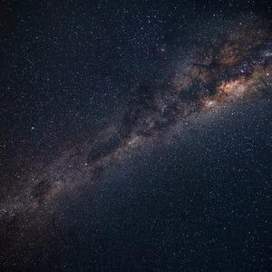 May include: A night sky filled with countless stars, showcasing the Milky Way galaxy. The image captures a dark blue expanse with a prominent, luminous band of stars and cosmic dust stretching across the frame.