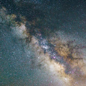 May include: A photograph of the night sky, showcasing the Milky Way galaxy. The image captures a vast expanse of space filled with countless stars, with a prominent band of light and color. The colors range from deep blues and greens to warm yellows and browns.