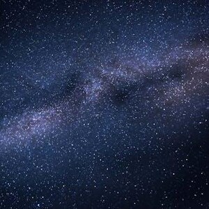 May include: A dark blue night sky filled with countless white and light blue stars. A bright, milky white and purple band of the Milky Way galaxy stretches across the image, creating a stunning celestial display.