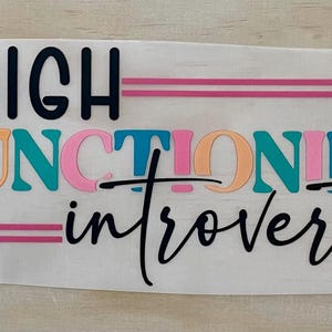 Peut inclure: Une tasse en céramique blanche avec une anse noire et l'inscription "But First, Coffee" en gras noir. La tasse est posée sur un fond flou, suggérant un cadre chaleureux.