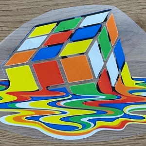 May include: A vibrant Rubik's Cube design with a melting effect. The cube's squares are in various colours, including red, blue, green, orange, yellow, and white. The melting effect creates a colourful, abstract design, with the colours flowing downwards.