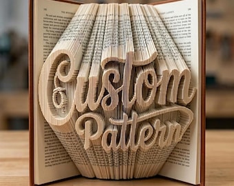 May include: A book sculpture featuring folded pages that form the words Custom Pattern in a cursive script. The book has a brown cover and is open to display the intricate paper folding technique used to create the three-dimensional text effect.