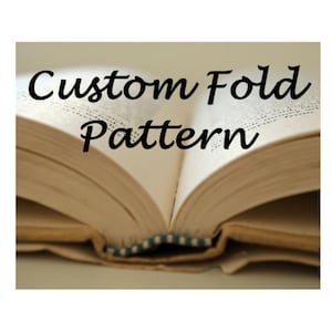 May include: An open book with the text "Custom Fold Pattern" in black script across the top. The pages are a warm beige color, and the binding is visible at the bottom.