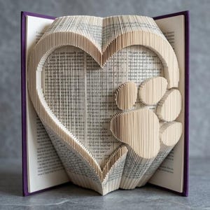 May include: A book with pages folded to create a heart shape and a paw print. The book has a purple cover and the pages are beige. The heart and paw print are the focal points of the design, showcasing a unique book art piece.