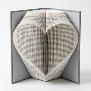 May include: A grey hardback book with pages folded to form a heart shape. The book is open, displaying the heart design in the centre. The pages are filled with printed text, and the book is set against a white background.