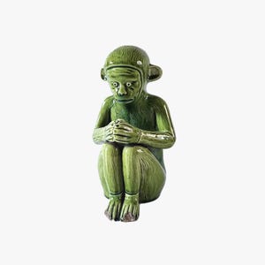 May include: A green ceramic monkey figurine in a seated pose, with hands clasped. The monkey has a detailed face and a glossy green finish. The figurine is a decorative item, suitable for display.