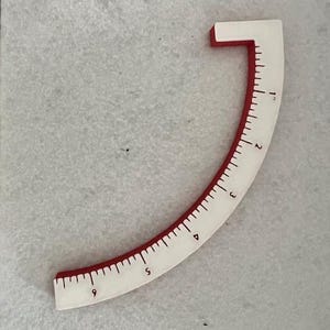以下が含まれることがあります： インチの目盛りが付いた、白と赤の曲線定規。定規は四半円の形をしており、赤い縁があります。定規には1から9までの数字が表示されています。