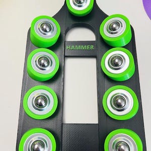 Può includere: Un telaio nero ad arco con dieci cuscinetti a rulli verdi e argentati. La parola "HAMMER" è stampata in verde sul telaio. I rulli sono distanziati uniformemente e sembrano essere in plastica e metallo.
