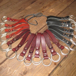 May include: A set of leather key fobs with metal rings. The fobs are in three colors: red, brown, and black. Each fob has a metal rivet.