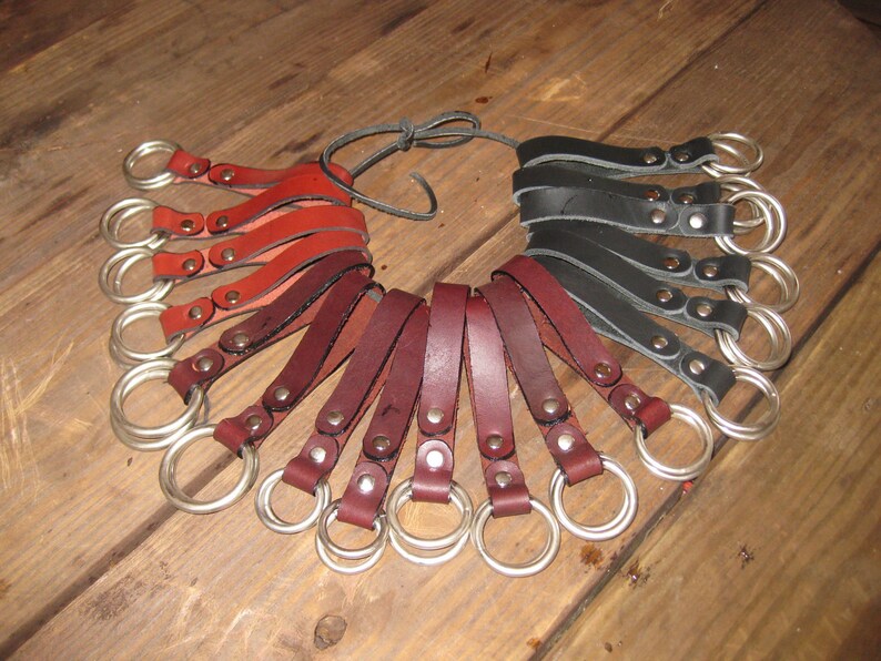 May include: A set of leather key fobs with metal rings. The fobs are in three colors: red, brown, and black. Each fob has a metal rivet.